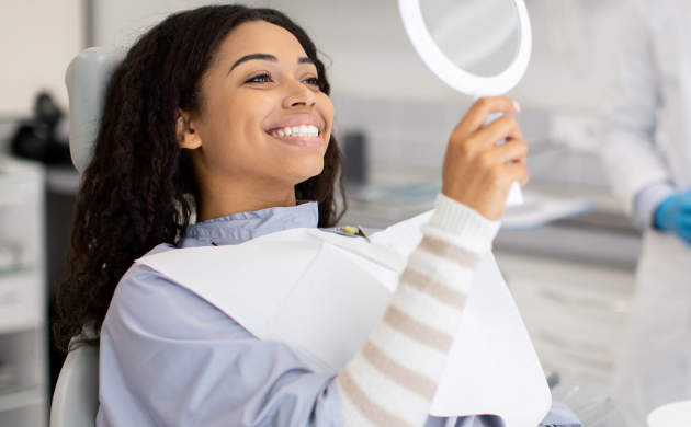Woman holding dental mirror in modern dental office, smiling at her reflection.
