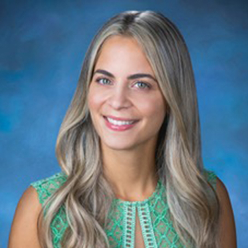 Young woman smiling at camera, professional headshot against blue background for dental practice.